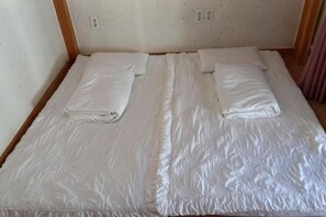 A double bed with white bedding, a wooden headboard, and a plain wall with electrical outlets. - Adam Guesthouse (Gyeongju)