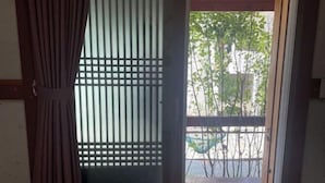 Una habitación con puerta corredera que da a un espacio exterior con terraza de madera y una silla verde.