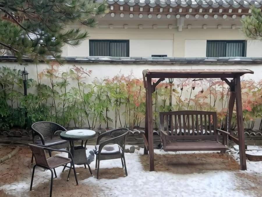 A patio with a wooden swing, two chairs, and a table.