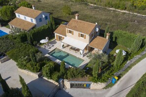 Une maison à deux étages avec une piscine, entourée de verdure et d’un mur de pierre.
