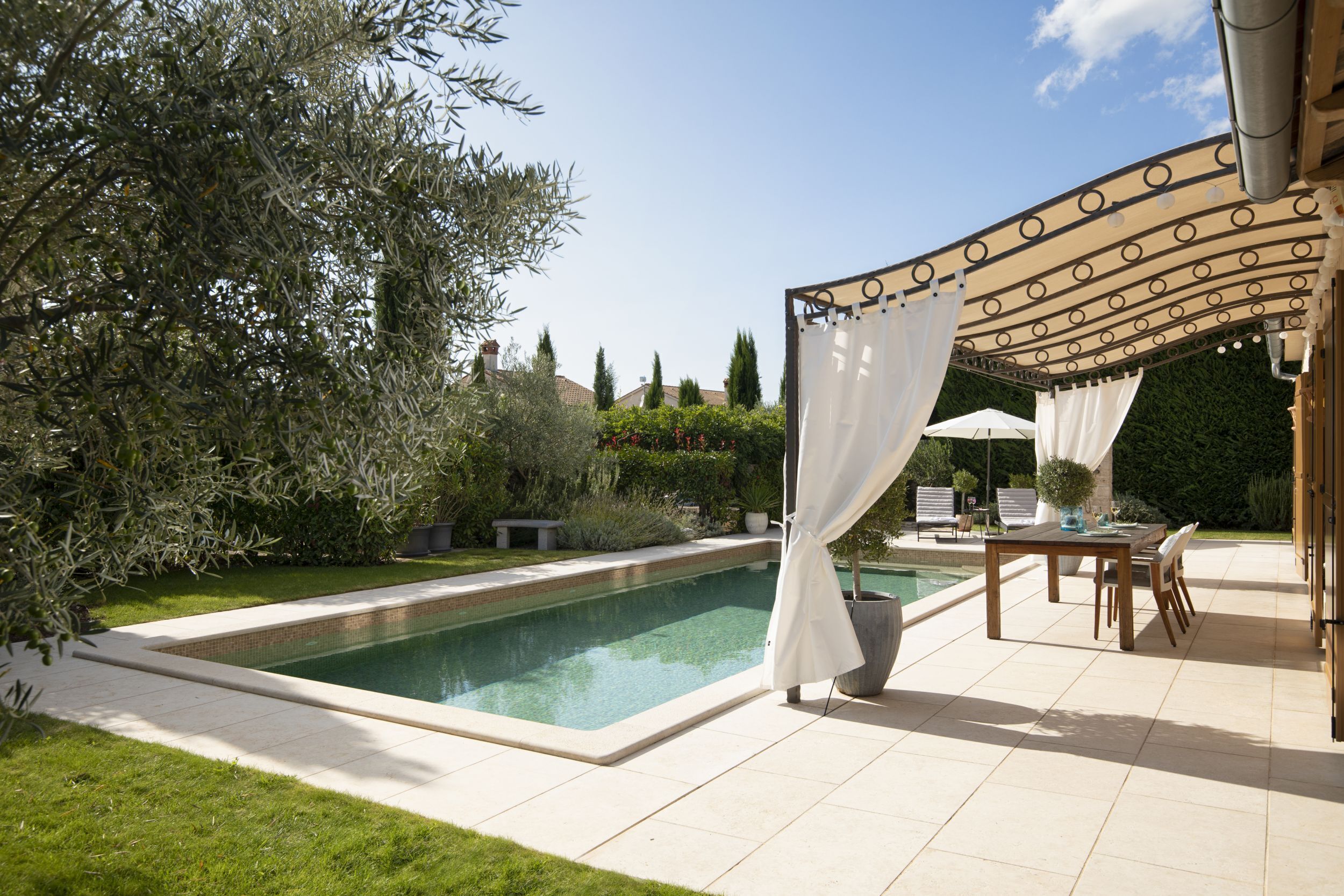 Una piscina con una pérgola y zona de estar al aire libre.
