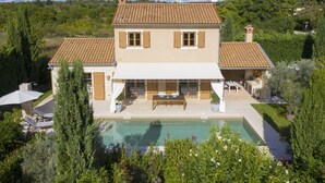 Una casa de dos pisos con piscina, un patio con mobiliario exterior y un jardín.