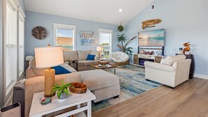 Una sala de estar con sofá, sillones, una mesa de centro y televisor. Incluye elementos decorativos como una lámpara, una planta y arte en la pared.