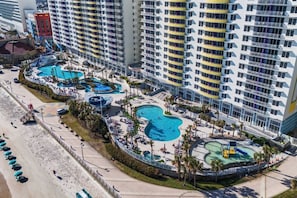 A high-rise hotel with multiple swimming pools, a beach area, and a lifeguard tower.
