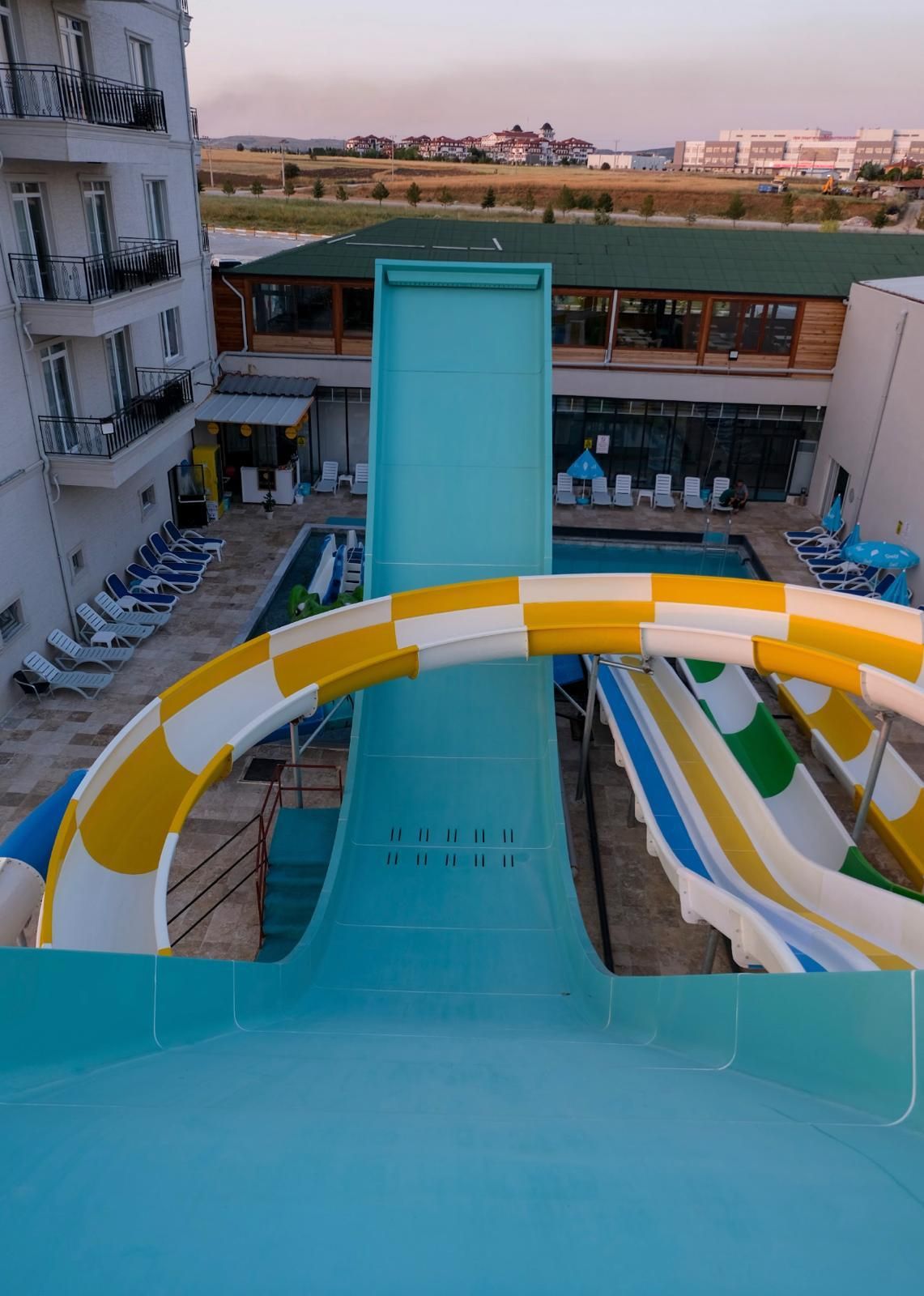 Un espace piscine doté d’un toboggan, de chaises longues et d’un bâtiment avec des balcons.