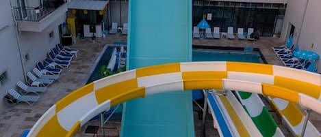 A pool area with a water slide, lounge chairs, and a building with balconies.