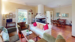 Un salon spacieux avec un canapé blanc, des fauteuils marron, une table basse en verre et une cheminée.