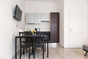 Une cuisine compacte comprenant une table et des chaises, un téléviseur à écran plat fixé au mur et un réfrigérateur.