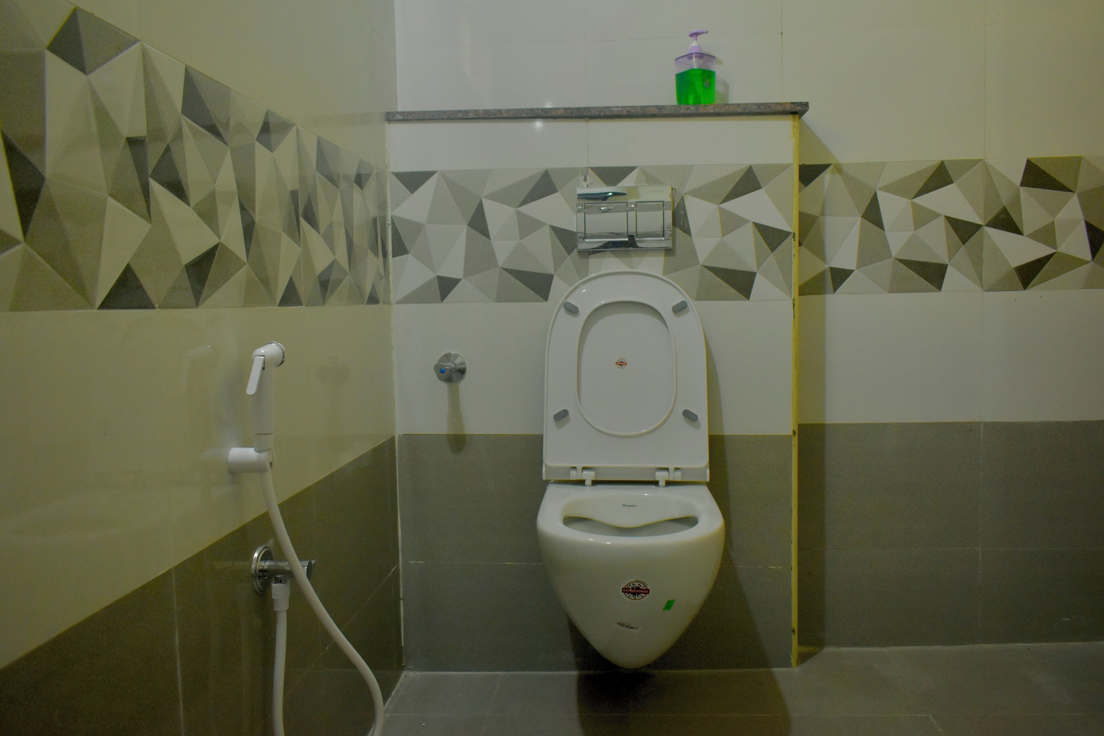 A bathroom with a toilet, a hand dryer, and a soap dispenser on a shelf.