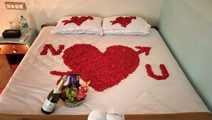 A bed with rose petals arranged in a heart shape, a bottle of champagne, a bowl of fruit, and two towels shaped like swans. - Gandhada Goodu Retreat (Kanakapura)