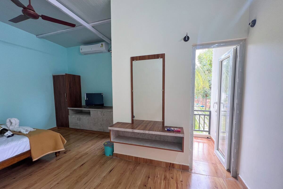 A bedroom with a bed, a wooden desk, a mirror, and a window.