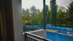 A pool with a blue and white tiled edge, surrounded by lush greenery and palm trees. - Gandhada Goodu Retreat (Kanakapura)