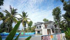 A two-story building with a balcony, surrounded by palm trees and a swimming pool. - Gandhada Goodu Retreat (Kanakapura)