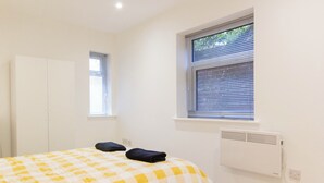 A bedroom with a checkered bedspread, a radiator, a window with blinds, and a wardrobe.
