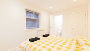 A bedroom with a checkered bedspread, a window with blinds, a radiator, and a white door.