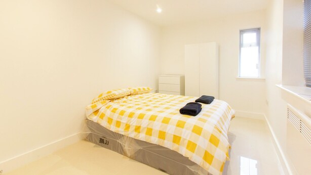 A small, clean room with a bed, a small bedside table, and a window.