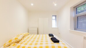 A bedroom with a checkered bedspread, a bedside table, a wardrobe, and a window with blinds.