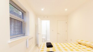 A bedroom with a checkered bedspread, a radiator, a window with blinds, and a door leading to a bathroom.