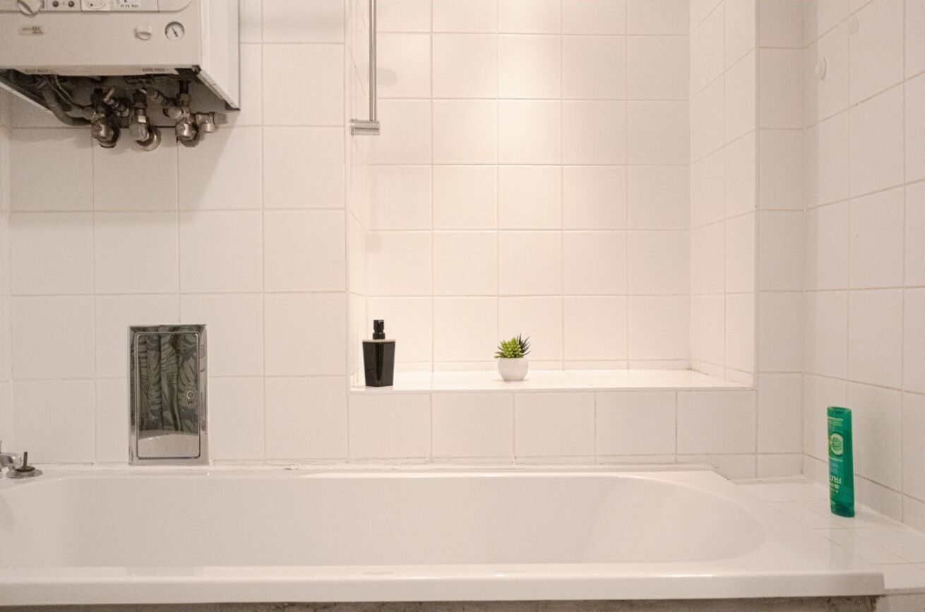 Een badkamer met een bad, een klein plankje met een plant en een fles, en een douchehoek.