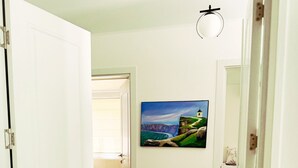 A hallway with a wooden floor, a striped rug, a painting of a coastal landscape, and a white door. - Pensiunea Casa Veche Butuceni Orheiul vechi. (Butuceni)