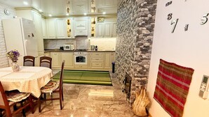 A kitchen with white cabinets, a stone wall, a clock, and a dining area with a table and chairs. - Pensiunea Casa Veche Butuceni Orheiul vechi. (Butuceni)