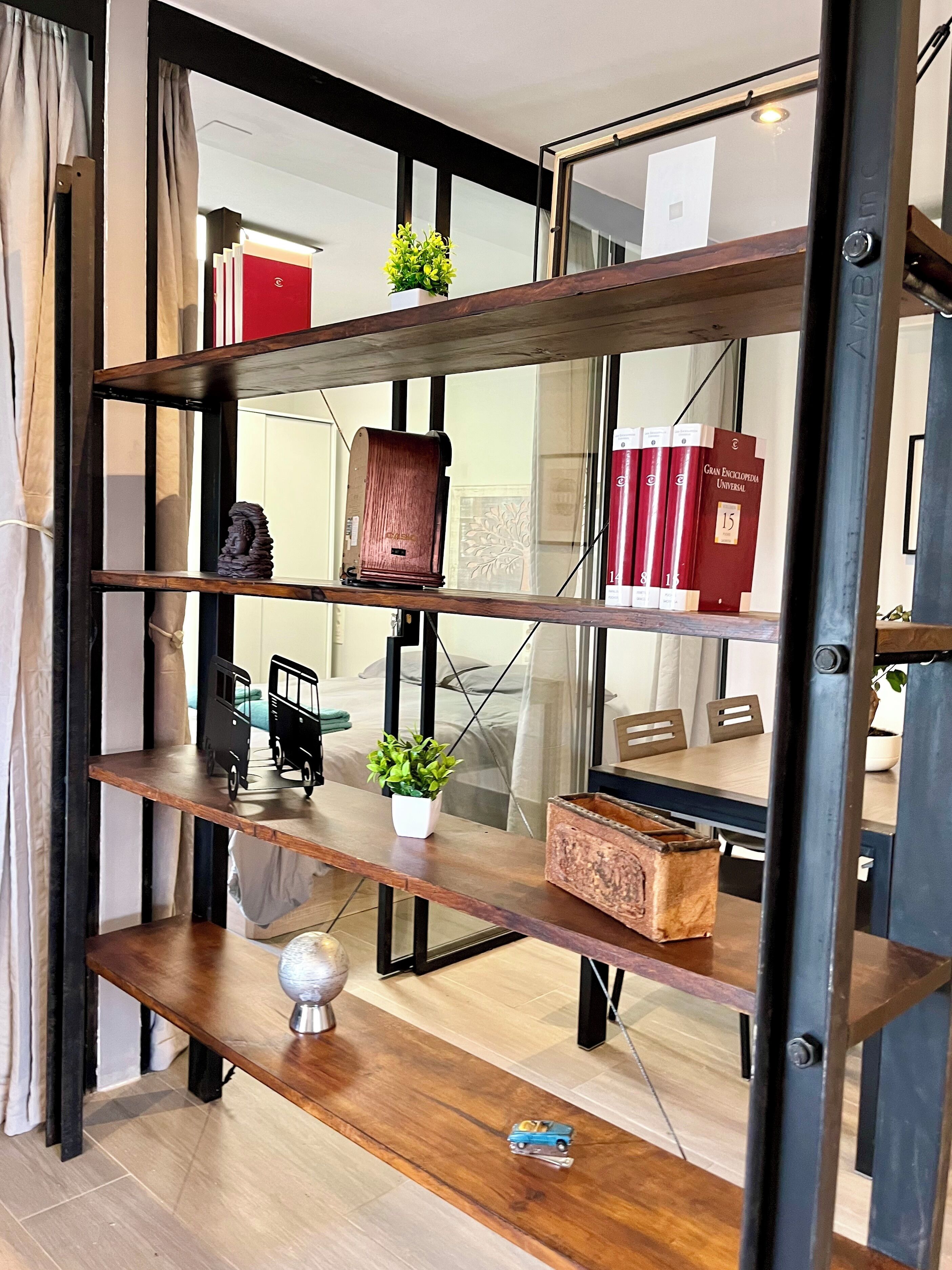 Una estantería de madera escalonada con diversos objetos decorativos, como libros, una pequeña estatua y un coche de juguete.
