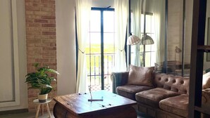 Un salon avec un mur en briques, une grande fenêtre avec des rideaux, un canapé marron, une table basse en bois et une plante en pot.