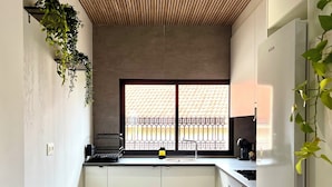 Une cuisine moderne avec un plafond en bois, une fenêtre agrémentée d’un paravent décoratif et un évier.