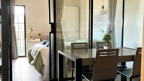 Un espace repas moderne avec une table et des chaises en bois, une plante en pot et une vue sur une chambre à coucher avec un lit et des rideaux.