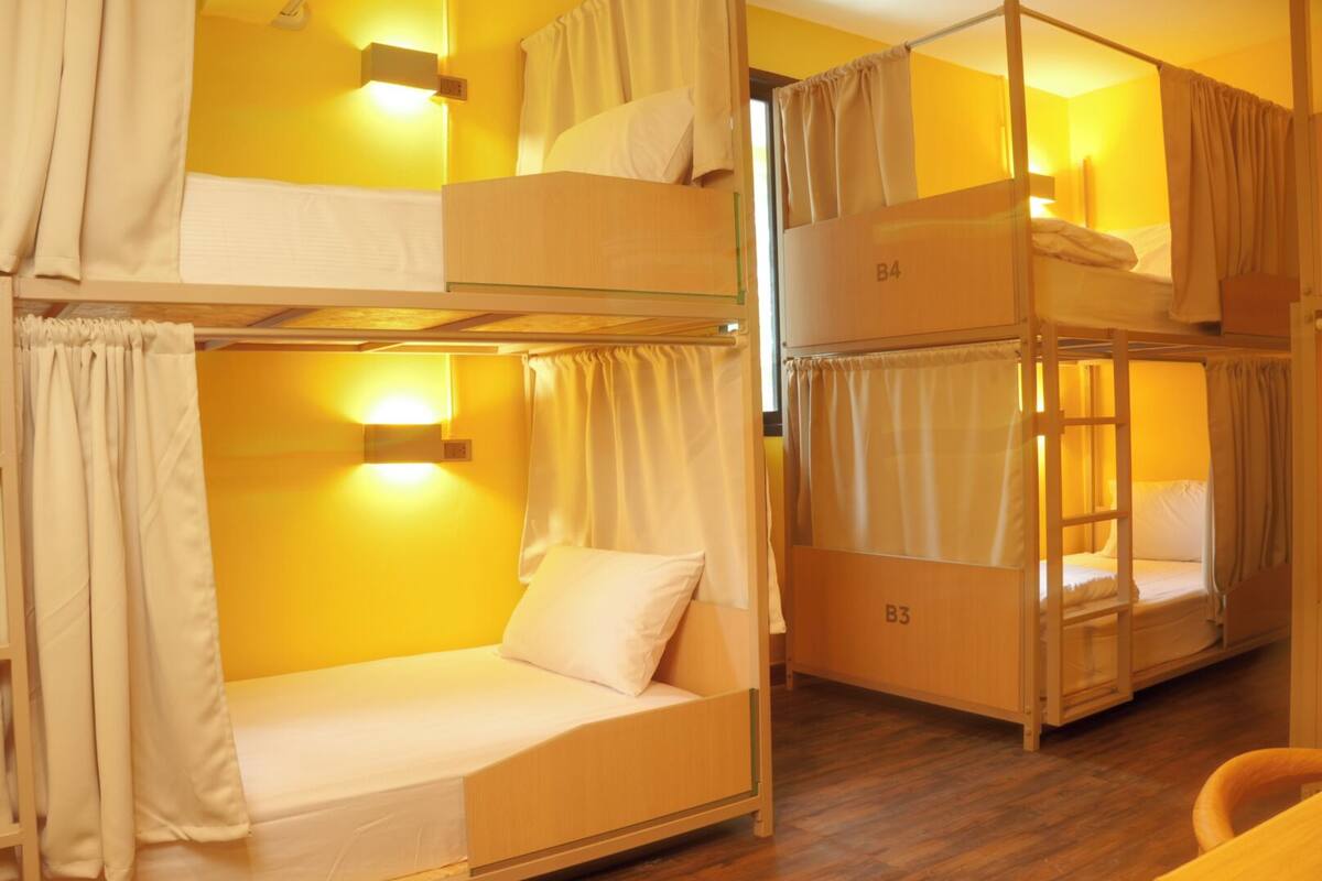 Habitación tipo dormitorio con literas, cada una identificada con un número, y una pequeña mesa con una silla.