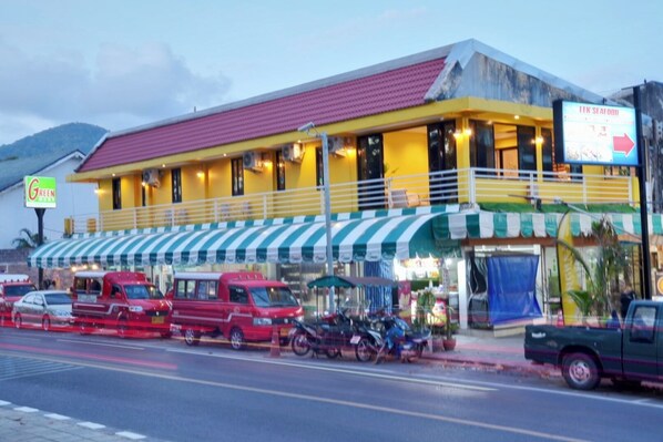 A two-story building with a yellow facade and a red roof, featuring a green and white striped awning.