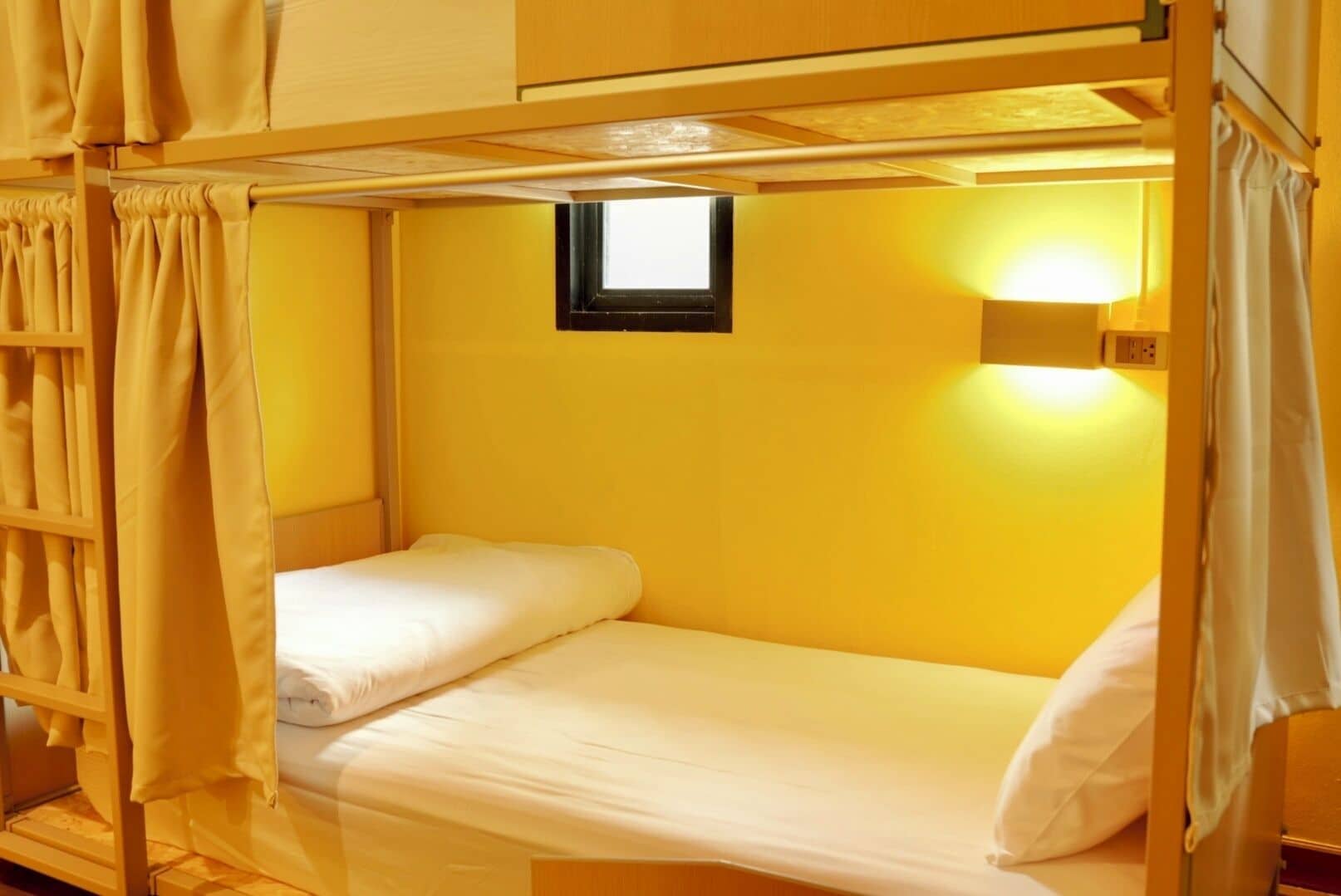 A bunk bed with a small window, a wall-mounted light, and curtains.