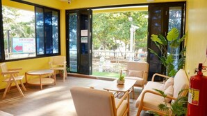 A room with a wooden floor, a sofa, a table, and chairs. There is a window with a view of trees and a sign outside.