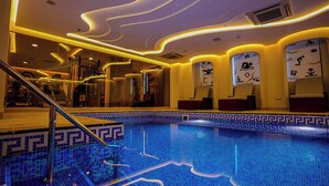 Una piscina con un diseño geométrico de mosaicos, barandilla de vidrio y una decoración interior moderna con líneas curvas y obras de arte en la pared.