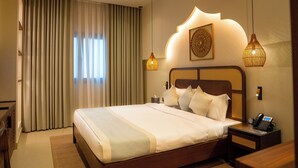 Una habitación de hotel con una cama grande, una mesita de noche con teléfono y una ventana con cortinas.