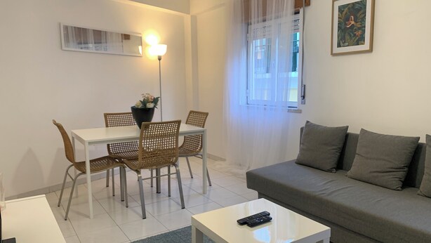 A living room with a grey sofa, a white coffee table, and a dining area with a white table and wicker chairs. - Vintage Chiado with Terrace (Lisboa)