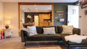 A cozy living room with a dark green sofa, a wooden coffee table, and a kitchen visible in the background. - Lower Well Farm House (Totnes)