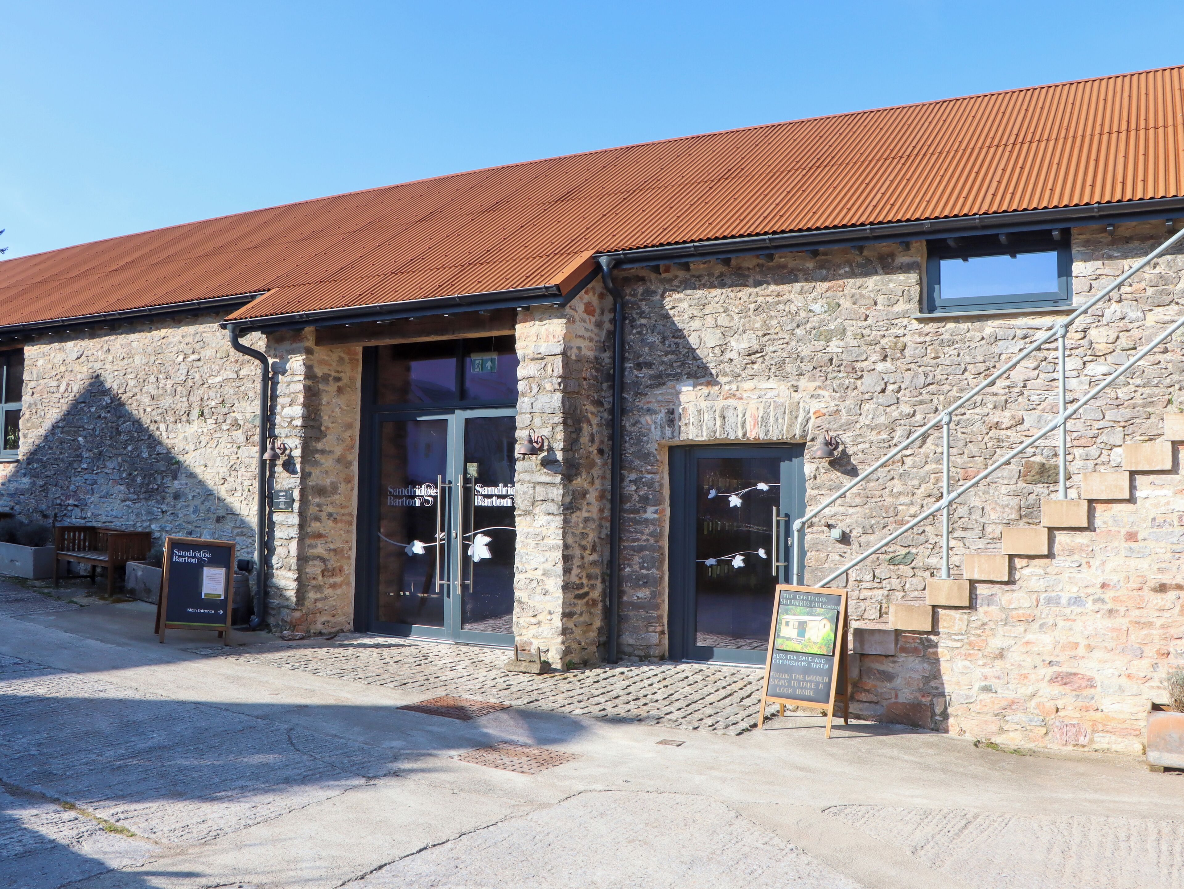A stone building with a metal roof, a staircase, and a bench outside.