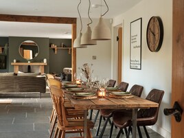 Un comedor con una mesa de madera dispuesta para seis personas, rodeada de sillas de cuero. En la pared, un reloj grande y una cita enmarcada.
