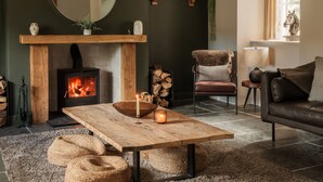 A cozy living room with a fireplace, a round mirror, a wooden table with candles, and a comfortable sofa. - Lower Well Farm House (Totnes)