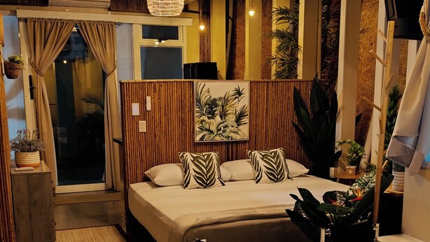 A modern bedroom with a large curved bathtub, a bed with leaf-patterned pillows, and a ceiling with wooden beams and a hanging light fixture. - Bungalow Arenal Dream View / Jacuzzi and hot springs (Palma)