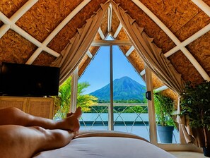 A room with a bed, a television, and a view of a mountain. - Arenal Bungalow: Stunning View / Jacuzzi and Hot Springs (Palma)