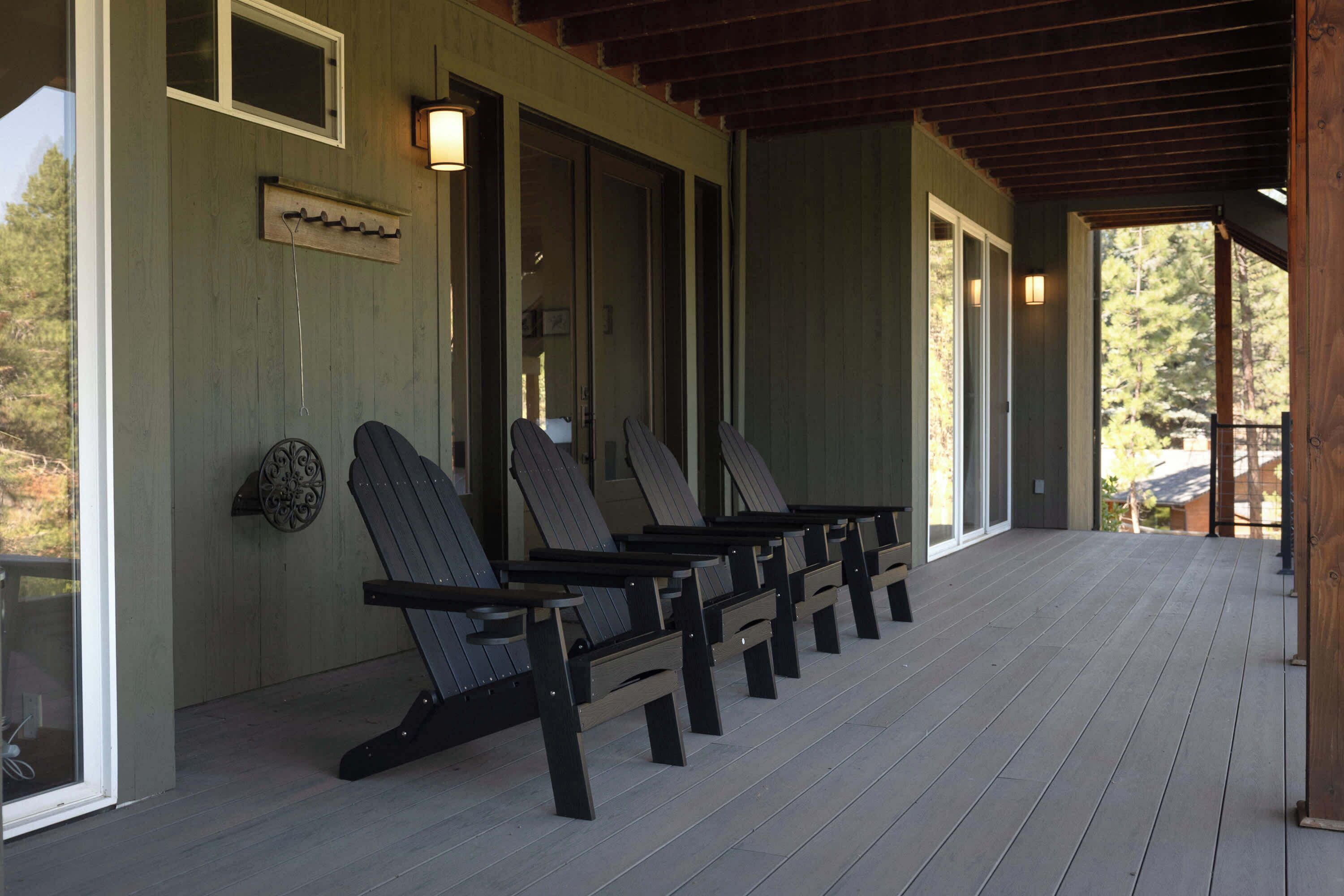 A covered porch with wooden chairs and a wooden bench, a wall-mounted light fixture, and a window with a view of trees.