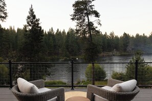 Eine Terrasse mit Korbmöbeln mit Blick auf einen See, der von Bäumen umgeben ist.