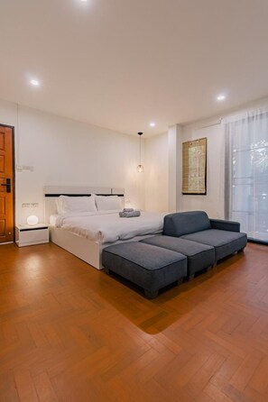 Ein modernes Schlafzimmer mit Bett, Nachttisch und grauem Sofa mit Poufs.