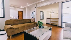 A modern living room with a brown sofa, a glass coffee table, and a white armchair. - Modern Family House - 4 Bedrooms 5 Mins From Old Town With Gallery - Deja Home (Chiang Mai)