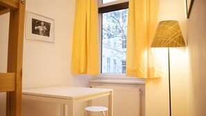 Une pièce avec un radiateur blanc, une table, un petit tabouret et un lampadaire.