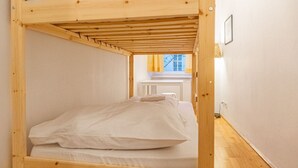 Une chambre avec un lit superposé, un plafond en bois, des murs blancs et une fenêtre avec des rideaux.