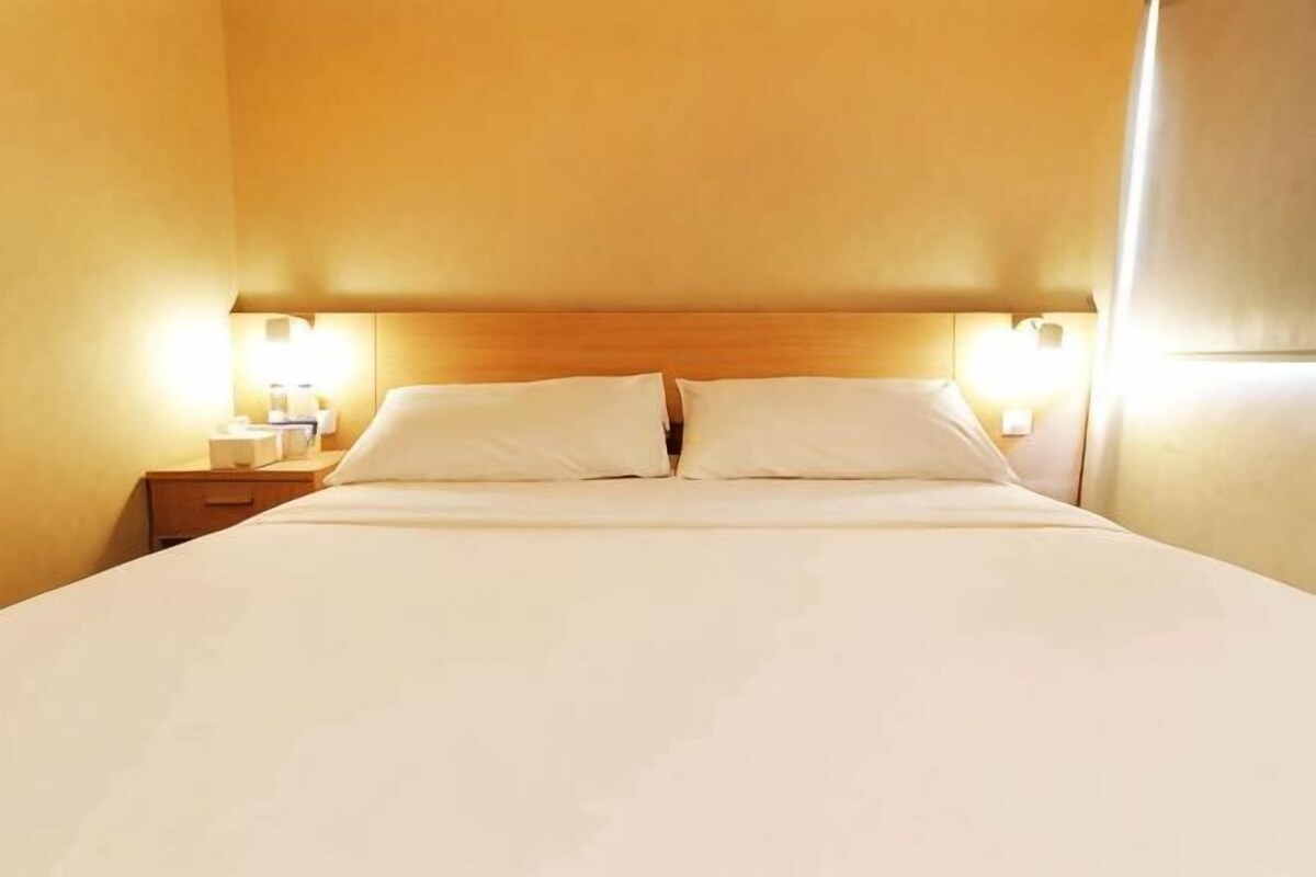 A hotel room with a large bed, two bedside lamps, and a wooden headboard.