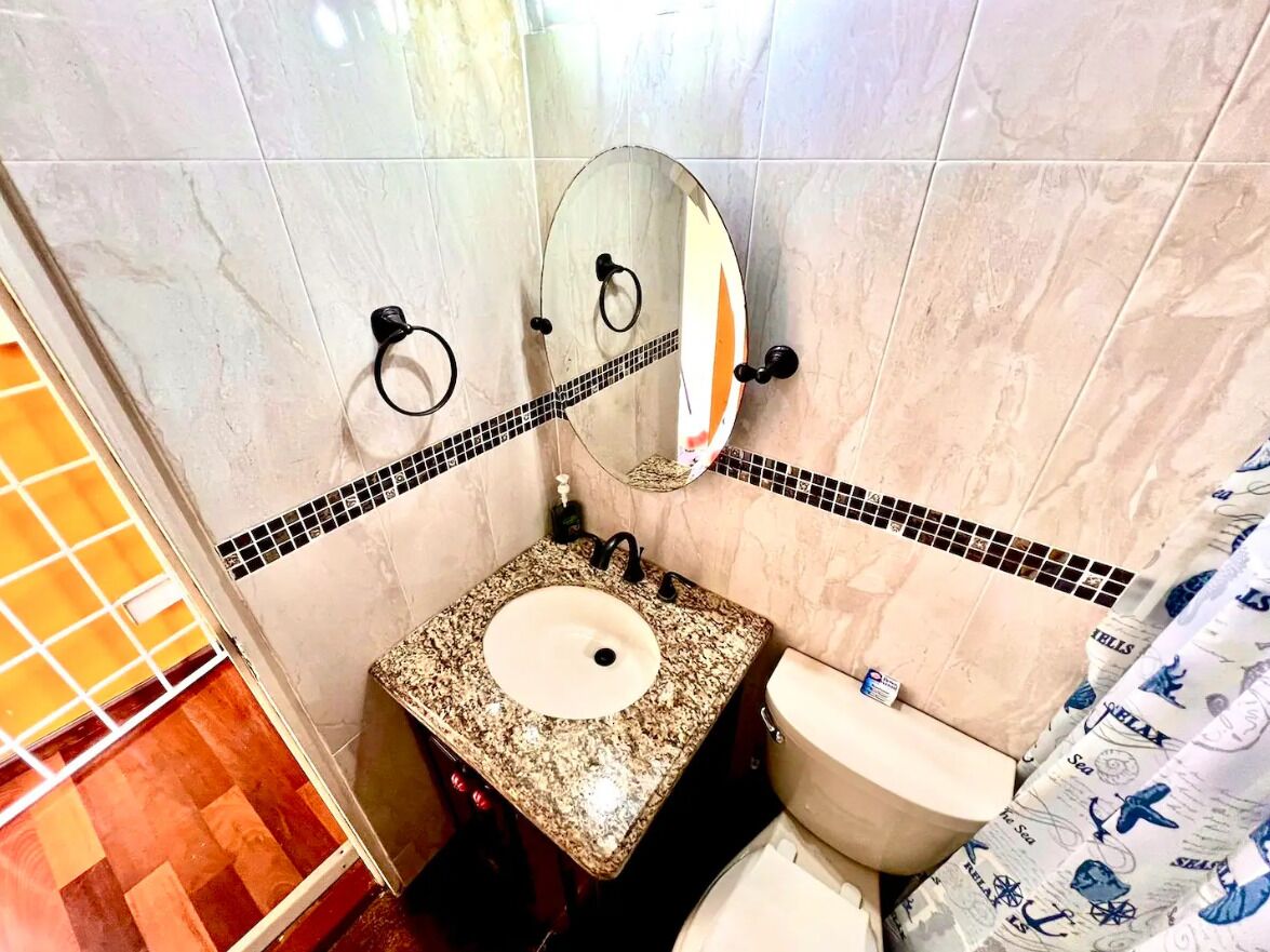 Un baño con lavamanos de granito, inodoro y espejo.